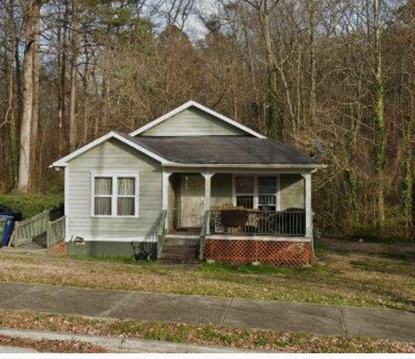 Small green bungalow with front porch on a wooded lot